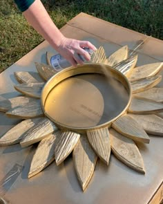 a person painting a metal sunflower on top of a cardboard box in the grass