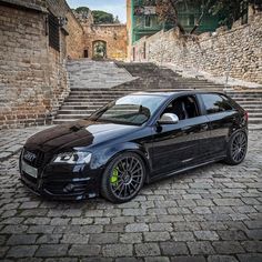 the black car is parked on the cobblestone road next to some stairs and stone steps