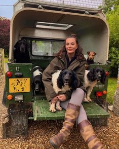 a woman sitting in the back of a green truck with four dogs on her lap