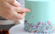 a woman is decorating a cake with sprinkles