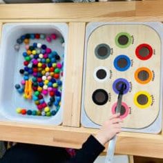 a young child is playing with toys in a wooden box that are filled with balls and crayons