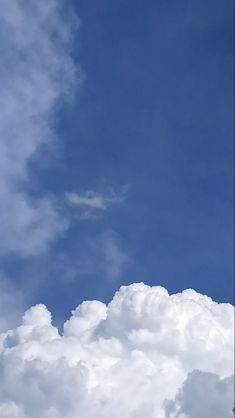 an airplane flying high in the sky with clouds behind it and trees on either side