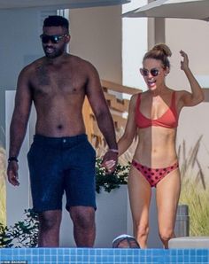 a man and woman in bikinis walking next to a swimming pool while holding hands