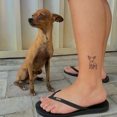 a small dog sitting next to a woman's foot with a tattoo on it