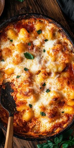 a casserole dish with cheese and spinach on the side next to a wooden spoon