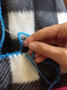 someone is knitting something blue on a plaid blanket