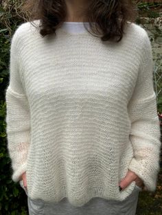 a woman standing in front of a bush wearing a white sweater