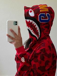 a person in a red hoodie holding a cell phone and wearing a shark mask