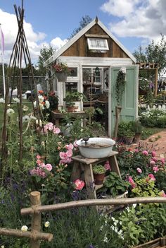 a garden filled with lots of flowers next to a small shed and fenced in area