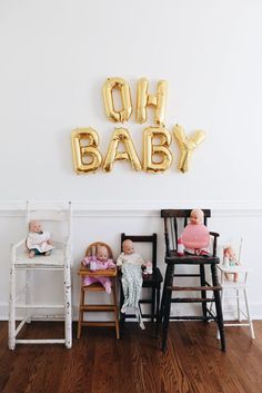 two baby dolls sitting on chairs in front of a wall with balloons that spell out the word oh baby