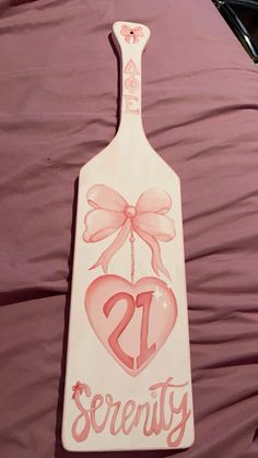 a wooden sign with a heart and bow hanging from it's side on a bed