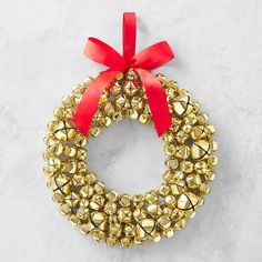 a gold wreath with red ribbon and bells hanging on the side of a white wall