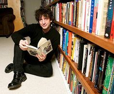 a man sitting on the floor reading a book in front of a bookshelf