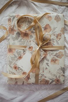 a gift wrapped in floral fabric and tied with gold ribbon on top of a bed