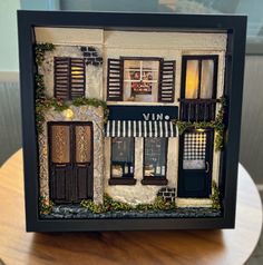 a doll house with shutters and windows is displayed in a shadow box on a table