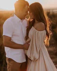 a man and woman standing next to each other in front of the sun at sunset