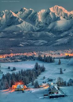 the mountains are covered in snow and lit up by street lights, with houses surrounded by pine trees