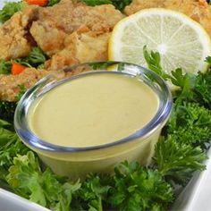 a white plate topped with chicken and salad next to a bowl of dressing on top of lettuce