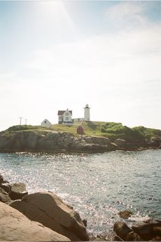 an island with a lighthouse on top of it next to the water and rocks in front of it