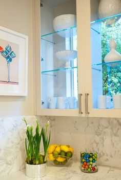 a kitchen with marble counter tops and white cupboards filled with colorful fruit in bowls