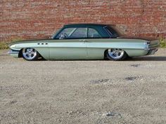 an old green car parked in front of a brick wall