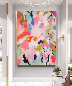 an abstract painting hangs on the wall next to a chair and table in a white room