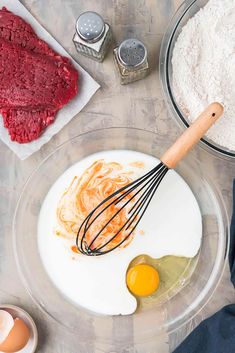 ingredients to make red velvet cake laid out in bowls on a wooden table, including eggs and flour