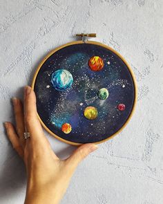 a hand is holding up a cross - stitch project with planets on it and stars in the sky