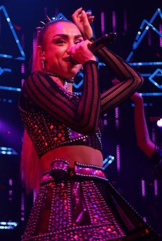 a woman in a disco outfit on stage with her hands up to the side, singing