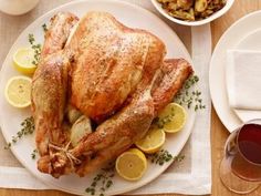 a whole chicken on a white plate with lemons and other food items around it