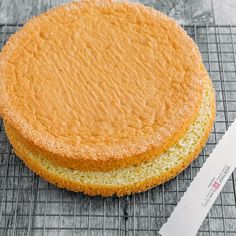 two cakes sitting on top of a cooling rack next to a paper and knife in front of them