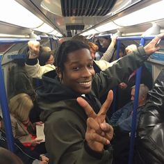 a man is smiling and giving the peace sign while riding on a train with his hands in the air