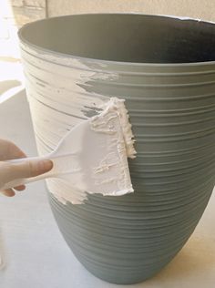 a person using a paint brush to paint a large gray vase with white stripes on it