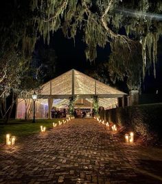 an outdoor wedding venue lit up at night with candles on the ground and trees in the background