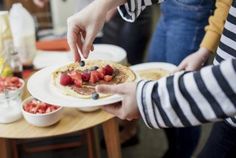 two people are serving pancakes with berries on top and yogurt in the middle