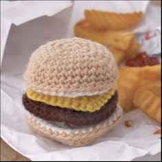 a crocheted hamburger sitting on top of a piece of paper next to fries