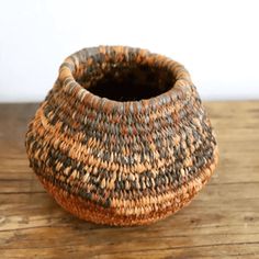 a woven basket sitting on top of a wooden table next to a vase with a black bottom