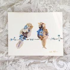 two birds sitting on top of a piece of paper with blue flowers in the middle