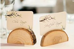 two place cards are placed on top of wood slices at the reception table with wine glasses in the background