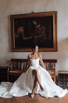 a woman is sitting on a bench in front of a painting and posing for the camera