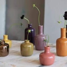 five different colored vases sitting on top of a marble table next to each other