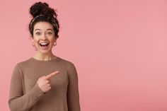 a woman pointing to the side with her index finger and smiling, on a pink background