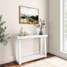 a white console table with vases and flowers on it in front of a window