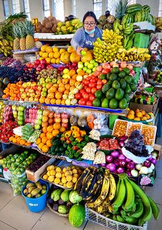 a woman standing in front of a large display of fruits and vegetables