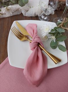 a white plate topped with a pink napkin and two gold utensils next to flowers