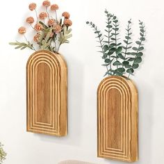 two wooden vases with flowers and greenery in them on the wall next to a chair