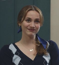 a woman wearing a blue and white sweater with a bow around her neck smiling at the camera