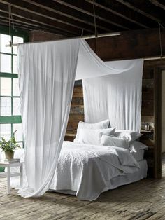 a canopy bed with white sheets and pillows in a rustic style bedroom, next to a window