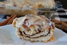 cinnamon roll with icing sitting on top of a white plate next to cinnamon sticks