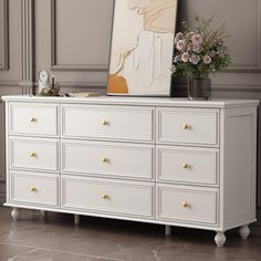 a white dresser with flowers and a painting on it